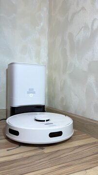 Robotic vacuum cleaner positioned near charging dock on wooden floor, showcasing gradual movement and proximity to wall, highlighting cleaning technology in action