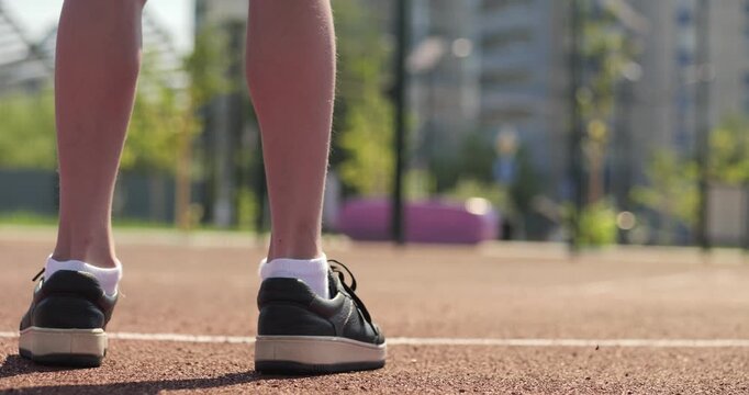 Close up of child legs on outdoor court in sunny day. Basketball moment shows focus and readiness before play. Minimal basketball scene highlights kids sport lifestyle. Child boy basketball player. - Powered by Adobe