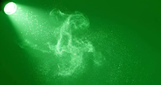 A green spotlight shines brightly on sparkling particles in a dark room creating a mesmerizing display of light and color with dramatic and theatrical and cinematic