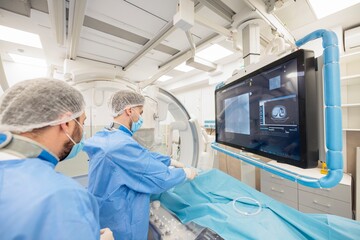 In a bright, high-tech surgical suite, a team of surgeons works diligently, monitoring screens and preparing for a crucial medical procedure while ensuring patient care