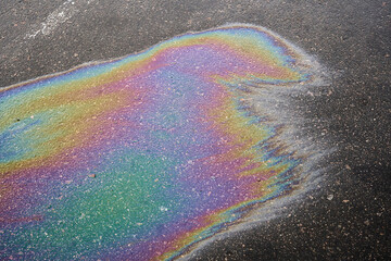 Oil slick creating a vibrant rainbow pattern on dark asphalt, showing pollution effects