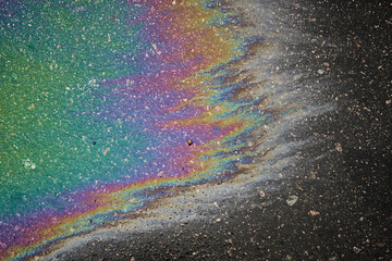 Oil slick on asphalt creating a vibrant rainbow of colors and reflecting light