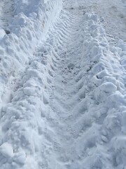 Car tire tracks in the snow, large snowdrifts in winter.
