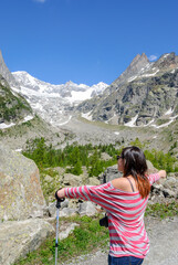 Female hiker enjoying alpine mountain scenery with snowcapped peaks and blue sky, standing on a trail during a summer hiking adventure.