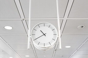 Minimalist office ceiling clock hanging on white grid ceiling. Modern interior time concept. Clean business environment. Simple geometry lines. Neutral corporate space with symmetry and light.