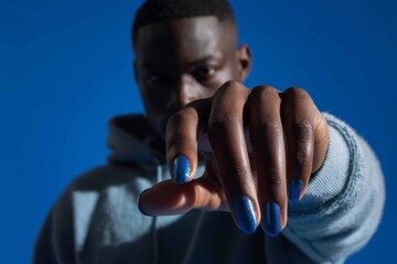 A man in a salon displays his hand with blue nail polish on one finger. He is engaged in a manicure session, showcasing his personal grooming choice