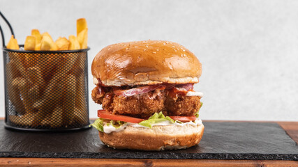 Crispy fried chicken burger with french fries served on slate board, fast food meal, restaurant food photography