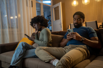 Young Black couple using smartphones separately, ignoring each other at home