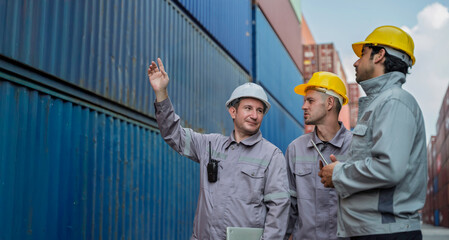 Team of professional logistic engineers inspecting shipping containers at a busy cargo port. Men pointing and discussing global export business plans using a digital tablet technology.
