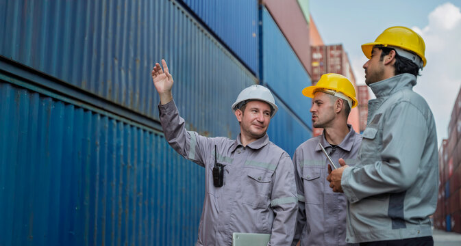 Team of professional logistic engineers inspecting shipping containers at a busy cargo port. Men pointing and discussing global export business plans using a digital tablet technology. - Powered by Adobe