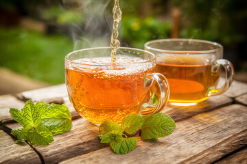 Two glass cups of hot tea with mint leaves on a wooden table outside in the garden