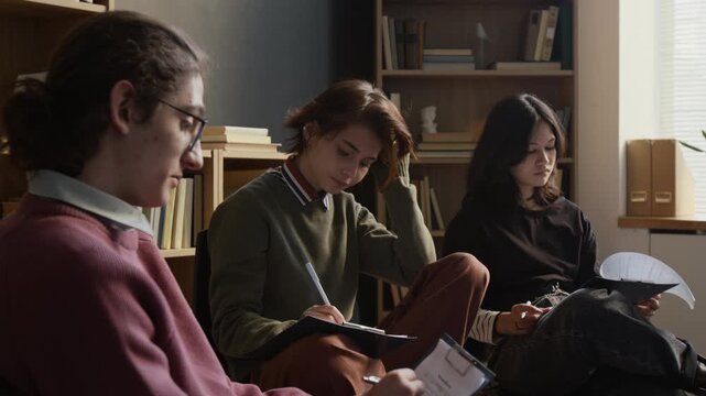 Group of young teenagers writing on clipboards filling out mental health tests during self assessment in therapists office