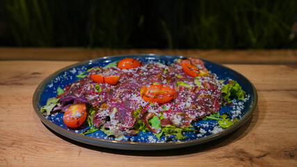 Beef carpaccio with fresh salad, cherry tomatoes and grated parmesan served on blue plate, gourmet Italian appetizer in fine dining restaurant