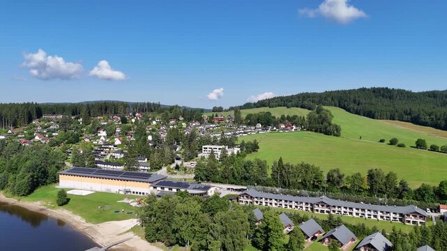 Lipno nad Vltavou, Czech Republic - July 19, 2025 - Aerial view of a lakeside village nestled among green hills and dense forests on a sunny day