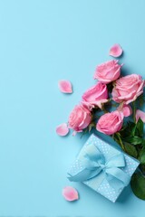 Mothers Day, Valentines Day, love holiday theme. A vibrant display of pink roses with lush green leaves and petals surrounding a blue gift box adorned with a blue ribbon.