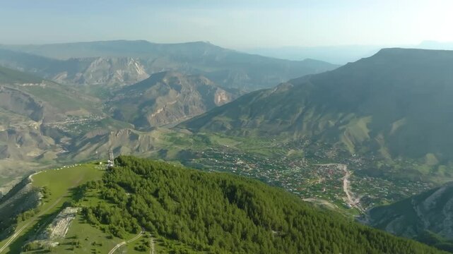 high-angle aerial shot captures the stunning natural beauty of the Zalala Ridge in the Republic of Dagestan, Russia. Lush green forests cover the slopes leading down to a picturesque mountain village 