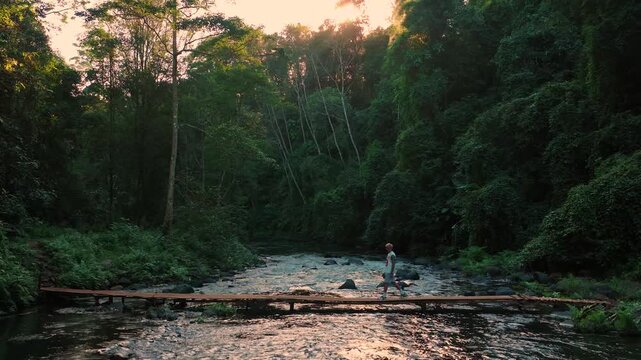 Man walking on wooden bridge near Phou Sawan waterfall in tropical forest, Pakse Laos