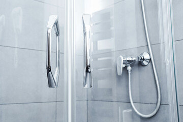 Glass shower door handles. Chrome bathroom fixtures on tiled wall. Modern walk in shower cabin. Clean hotel bathroom interior. Simple sanitary equipment. Vertical symmetry minimal design.