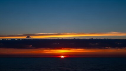 Obraz premium Vibrant Red Sun Setting on Ocean Horizon Under Layers of Dark Clouds