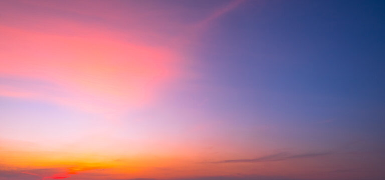 Beautiful sunset sky with colorful clouds in twilight. Panorama of dramatic orange, pink and blue sky background. Natural sunset landscape with vibrant sun light at evening