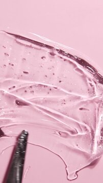 Smearing transparent serum gel on pink background with spatula. Hyaluronic acid and cosmetic background. Moisturizing texture cosmetics products concept.	
