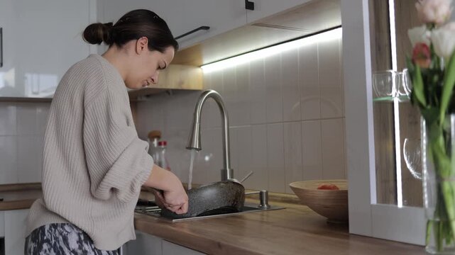 Woman washing frying pan in modern kitchen