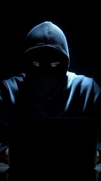 Una figura encapuchada frente a un ordenador, envuelta en misterio y oscuridad.