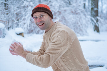 Happy Young man in orange jacket enjoying winter day, playing snowballs in snowy forest park, active outdoor leisure and fun, Playful moment in snow, weekend adventure, cold snowy day, winter walk