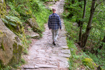 Young traveler man walks on old stone path through serene green forest, Italian Nature Hike, Exploring Ancient Trails, Hiker on historic pathway surrounded, Rural wilderness Journey