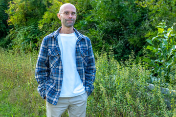 Smiling young bald man standing outdoors arms wide open enjoying nature wearing plaid jacket and white t shirt in sunny weather, Modern lifestyle portrait confident man, healthy lifestyle