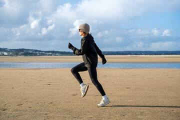 sporty woman running on a beach, winter fitness
