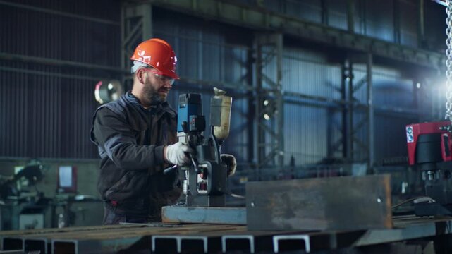 In the industrial factory blacksmith working with special machine to make some hole in the metal he wearing safety glasses and helmet