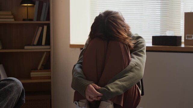 Medium shot of depressed teenage girl drawing knees to chest hiding face during group therapy session in college counselling room