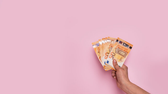 Horizontal web banner of a hand holding euro banknotes on a pastel pink background with copy space. Earn money, invest and save, cash concept