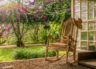 A vintage wooden rocking chair with a straw hat rests on a porch in a lush garden setting in Costa Rica. The scene has relaxation and vacation themes