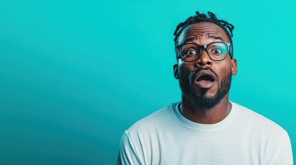 An expressive man displays a look of surprise with wide eyes and an open mouth, set against a bold turquoise background, capturing genuine emotion and reaction in a modern context.
