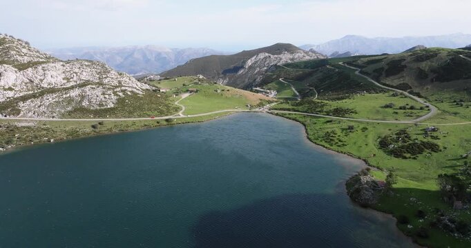 Drone orbit over Lago Enol, Covadonga, Asturias, Spain, crystal clear alpine lake surrounded by bright green mountain ridges and rocky outcrops