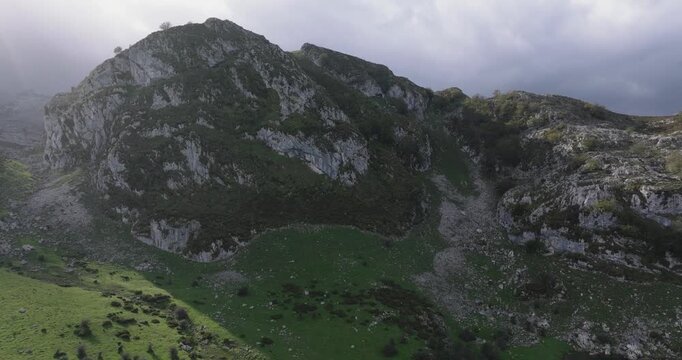 Drone aerial of Lago Enol, Covadonga, Asturias, Spain, moody sunlight hitting rugged cliffs and green valleys in Picos de Europa mountains