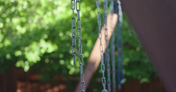 Metal swing set chains sway gently against a lush green background
