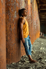 A young handsome man,an African model, walks alone, in a yellow T-shirt and jeans, in an unusual place
