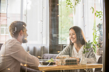 Happy young couple having animated conversation over coffee and breakfast at bright cafe