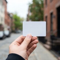 Hand holding blank white card in urban street setting.