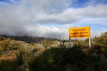 Translation: Military zone, no entry, danger of explosions. Information sign in a mountainous area, yellow in color, warning of the boundaries of a military exercise zone.