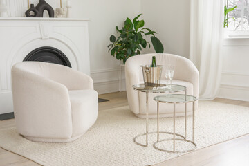 Minimalist living room with soft white armchairs, glass coffee table with ice bucket and glasses and elegant decor, creating cozy and stylish interior atmosphere with natural daylight.