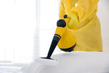 Pest control worker cleaning bed with steam cleaner indoors, closeup. Space for text