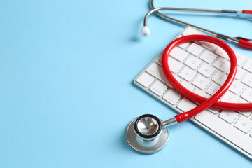 Telehealth. Keyboard and stethoscope on light blue background, closeup. Space for text