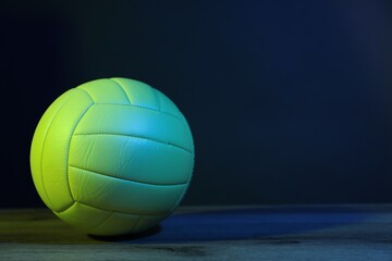 One volleyball ball on floor against dark background in color lights. Space for text