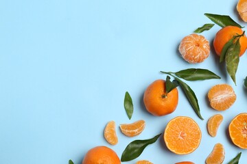 Fresh ripe tangerines and green leaves on light blue background, flat lay. Space for text