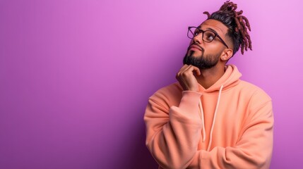 Fototapeta premium A thoughtful young man in a hoodie pondering ideas against a vibrant purple background, capturing the essence of introspection and modern lifestyle in a captivating light.
