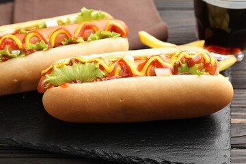 Tasty hot dogs with sauces, lettuce and potato fries on wooden table, closeup